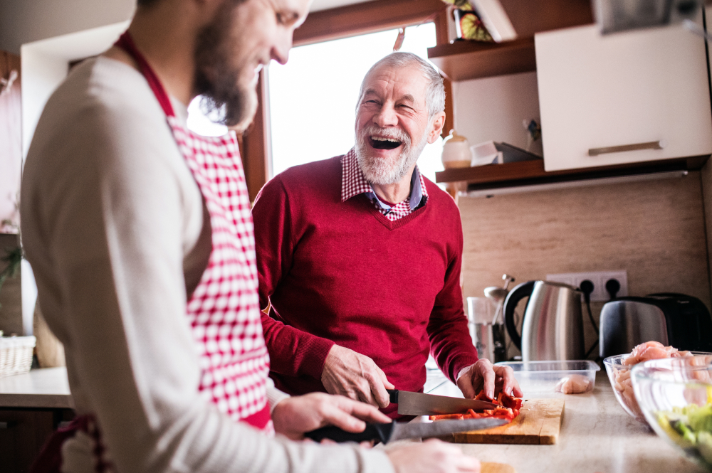 Young man and older man happily collecting vegetables in a community garden.